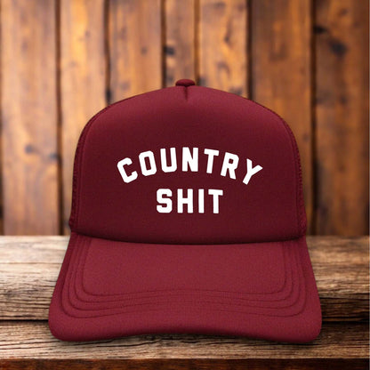 A two-toned vintage-style trucker hat with "Country Shit" in bold, distressed typography.