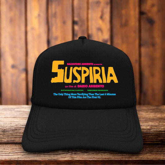 A dark trucker hat featuring a red foam front panel with the stylized, sharp "Suspiria" logo in a jagged, vintage font reminiscent of the 1977 horror film poster.
