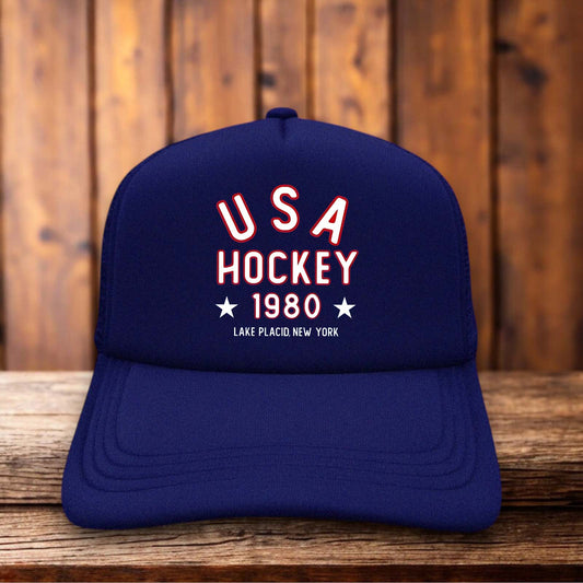 A retro trucker hat with a white foam front featuring the 1980 USA Hockey logo and "Miracle On Ice" text in red and blue vintage typography.