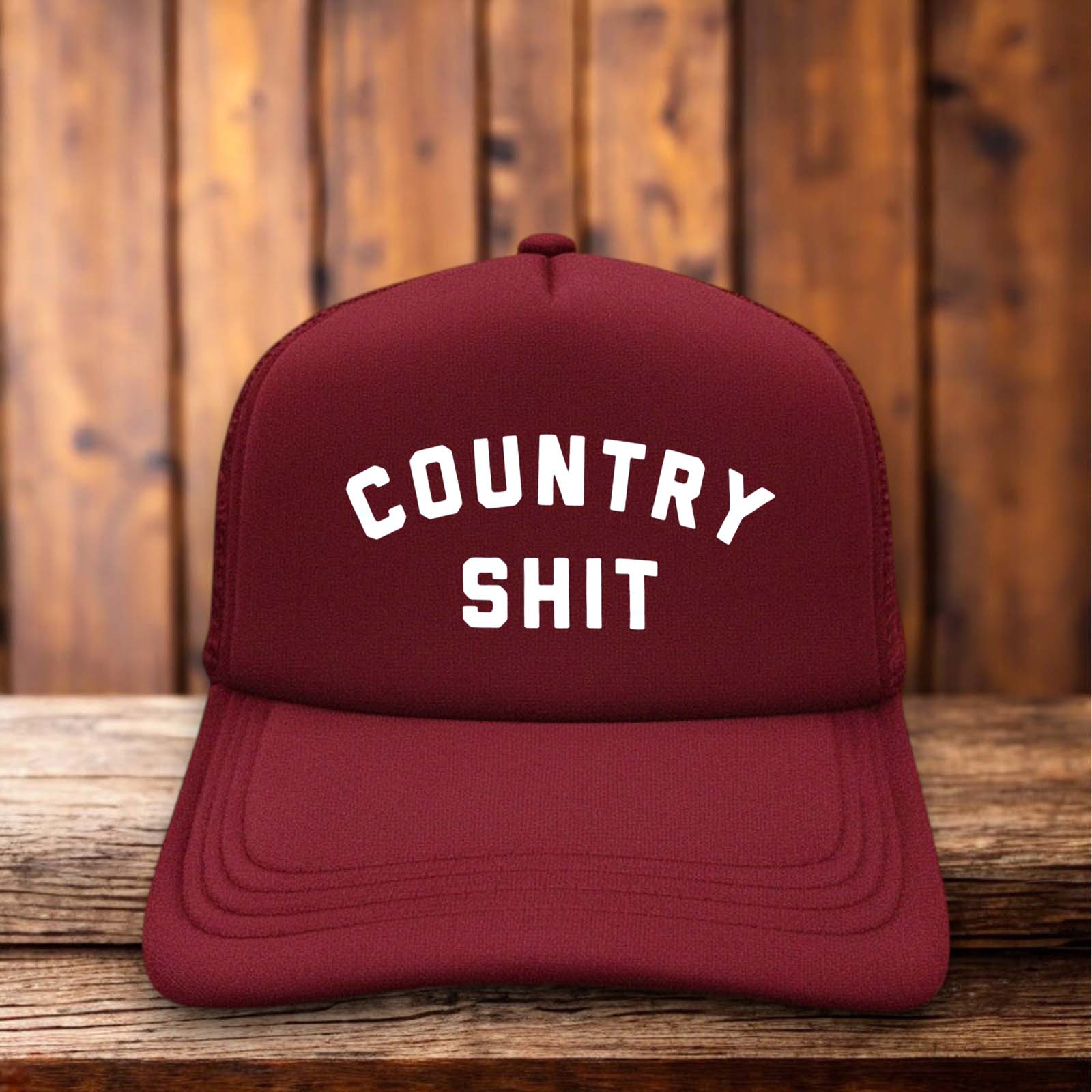 A two-toned vintage-style trucker hat with "Country Shit" in bold, distressed typography.