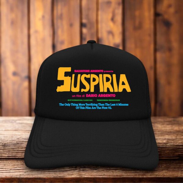 A dark trucker hat featuring a red foam front panel with the stylized, sharp "Suspiria" logo in a jagged, vintage font reminiscent of the 1977 horror film poster.