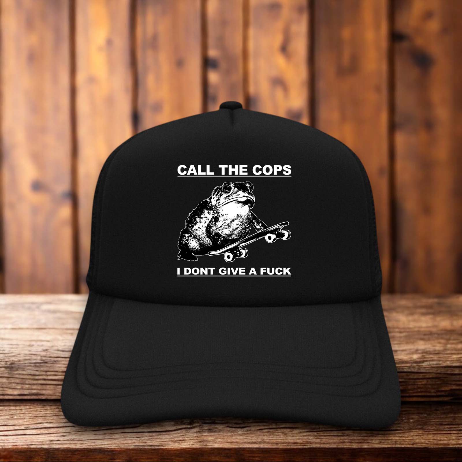 A white foam front trucker hat featuring a crude, cartoonish green frog sitting defiantly next to the bold, black text "Call The Cops I Don't Give A Fuck" in a simple sans-serif font.
